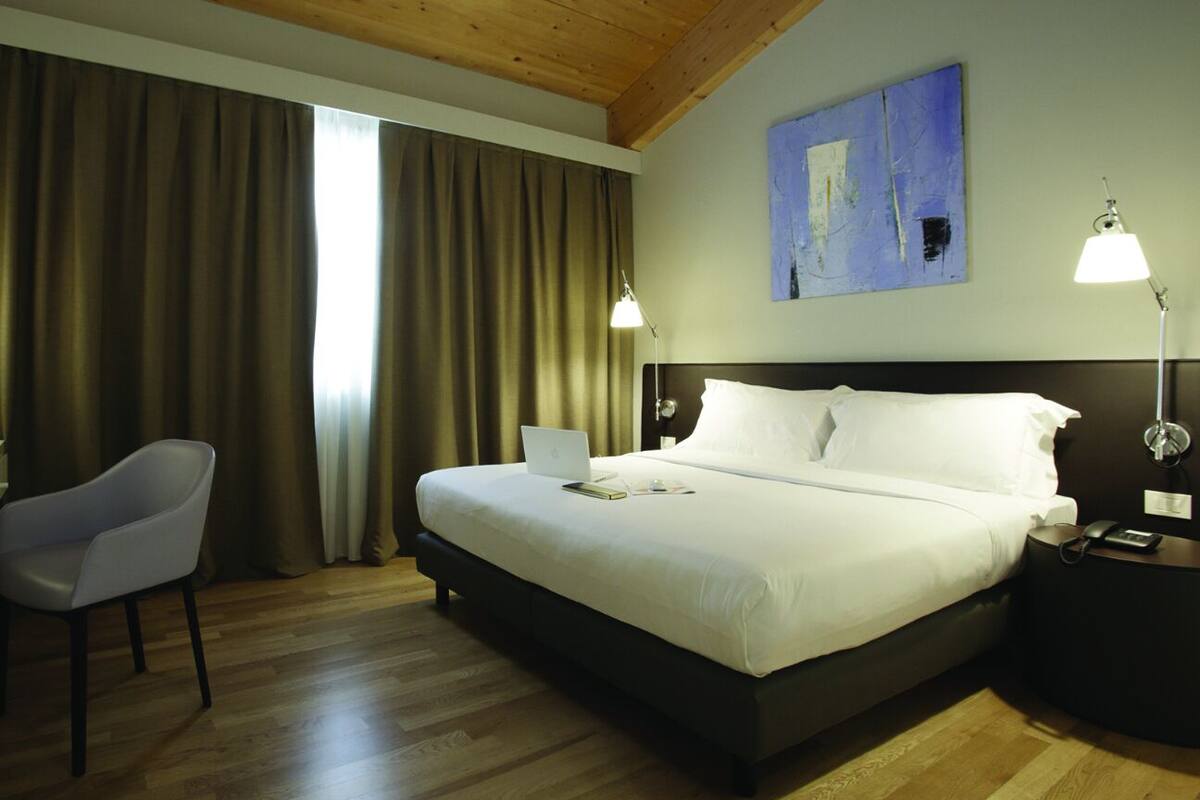 A hotel room with a bed, desk, chair, and two bedside lamps.