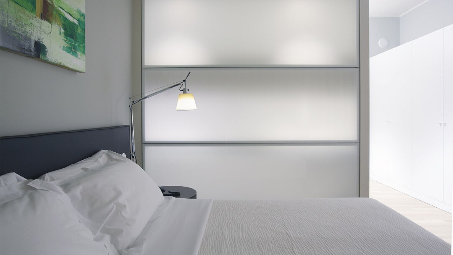 Una camera da letto moderna con un letto, una lampada da comodino, un comodino e un'ampia finestra.
