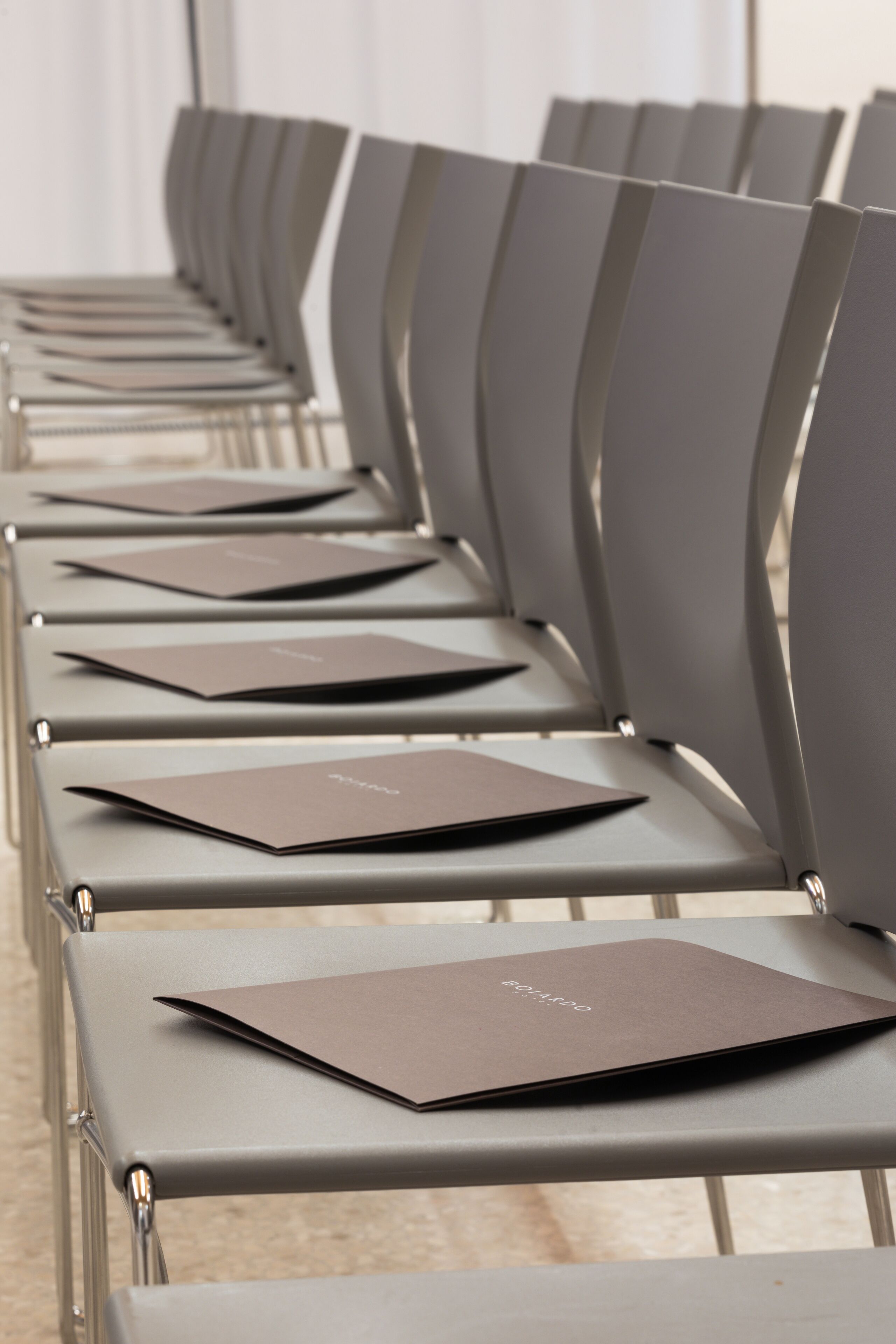 Rows of modern chairs with brown folders on them, arranged in a conference room setting.