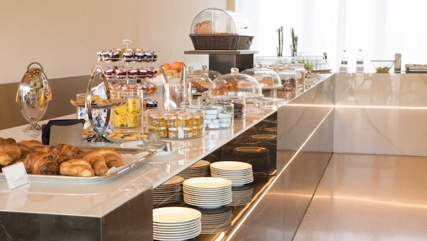 A buffet setup with various food items, including pastries, fruits, and condiments, arranged on a long counter with plates and serving dishes. - Boiardo Hotel (Scandiano)
