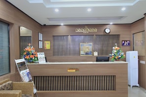 Un mostrador de recepción con detalles de madera, un reloj, certificados enmarcados y arreglos florales.