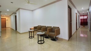 A spacious hallway with a seating area featuring wicker chairs and a small table, a ceiling fan, and a door at the end. - La Sara Vista (Bengaluru)
