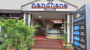 The entrance to Nandhana Palace hotel with a sign listing amenities like luxury rooms, banquet, A/C restaurant, and sweets on the ground floor. - La Sara Vista (Bengaluru)
