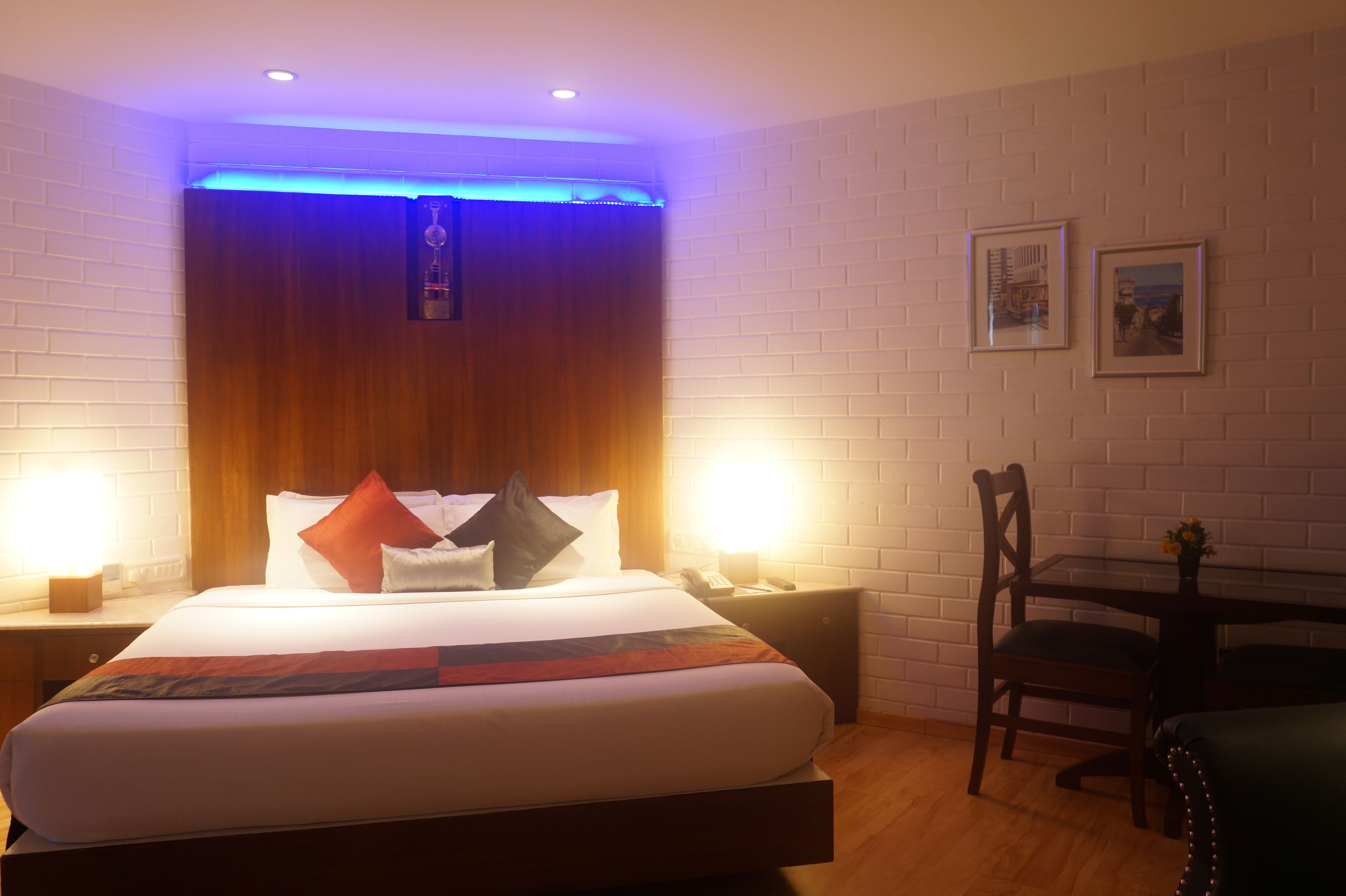 Habitació d'hotel amb un llit gran, capçalera de fusta, dues taules de nit amb làmpades, escriptori amb cadira i quadres amb marc a la paret.