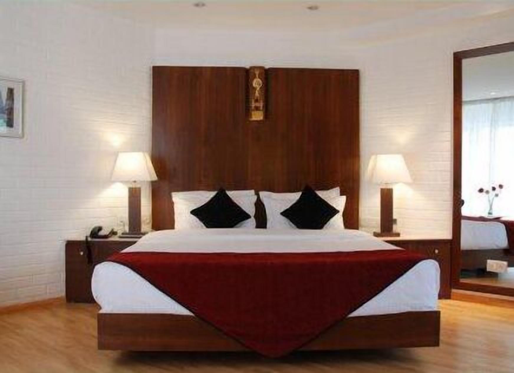 A hotel room with a large bed, two bedside lamps, a wooden headboard, and a mirror on the wall.