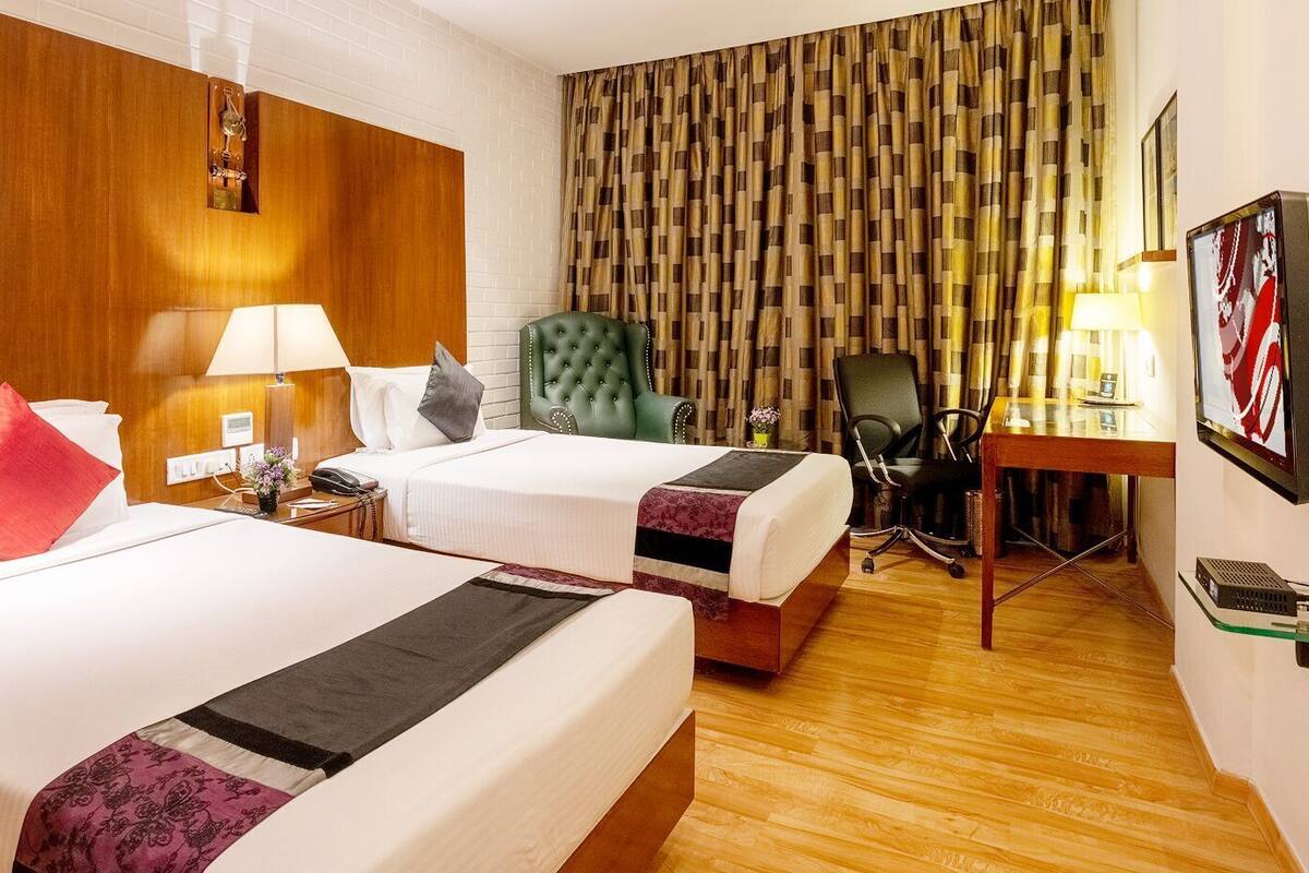 A hotel room with two beds, a desk, a chair, and a television.