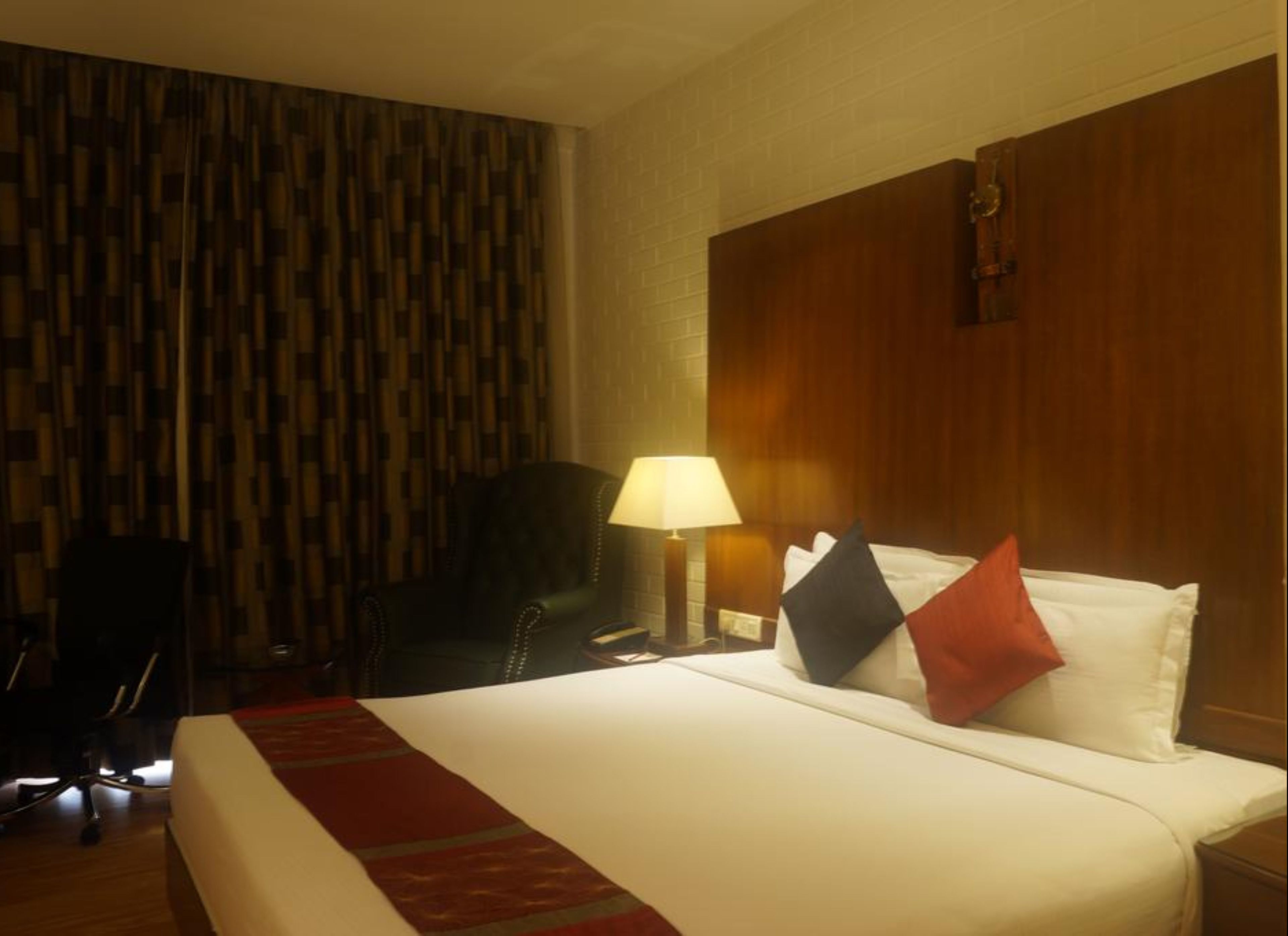 A hotel room with a large bed, a desk with a lamp, a chair, and a patterned wall.