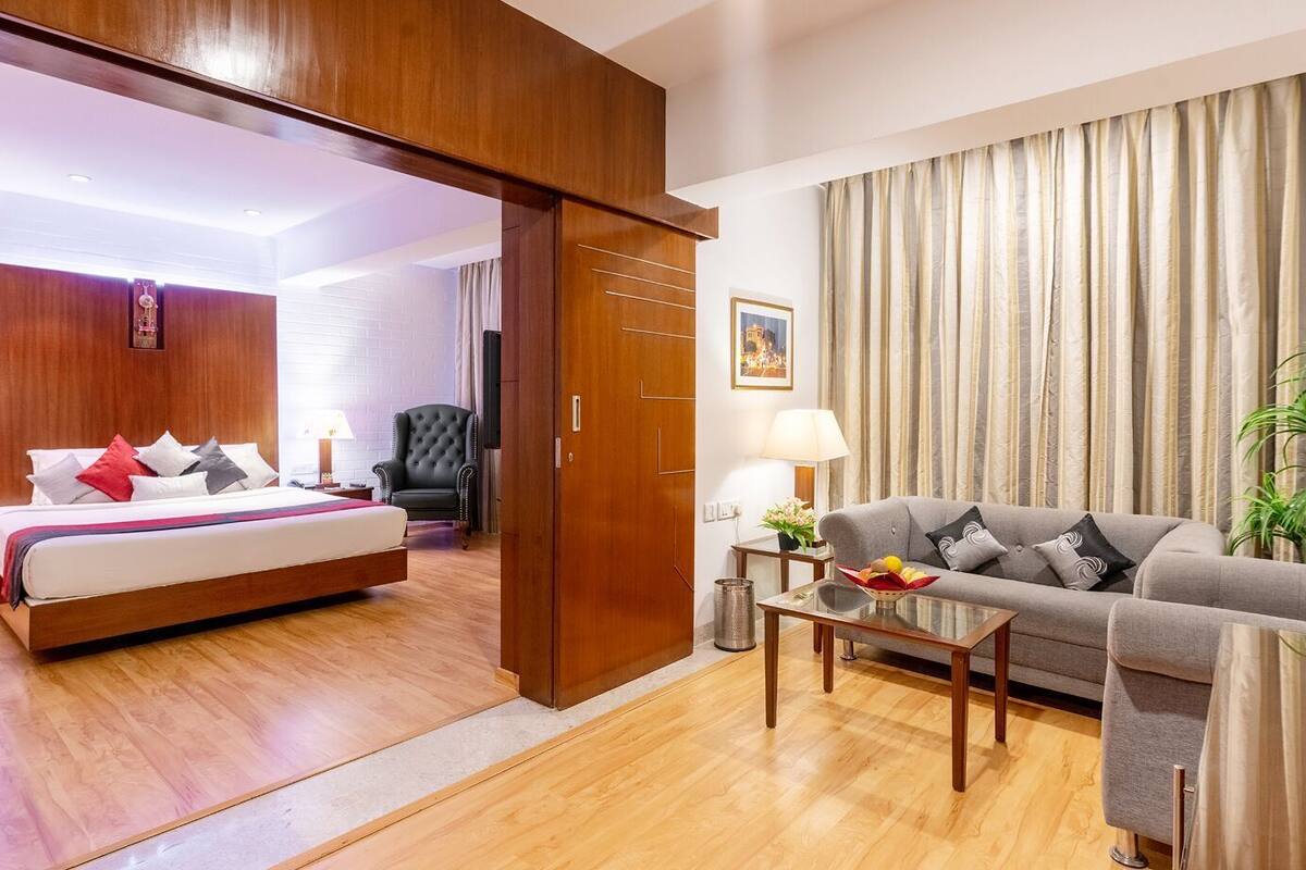 A hotel room with a bed, a sofa, a coffee table, a chair, and a curtain.
