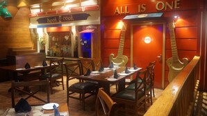 An interior with wooden tables and chairs, a 'hook & cook' sign, and a 'hard rock' logo. - SFO Hotel and Suites (Bengaluru)