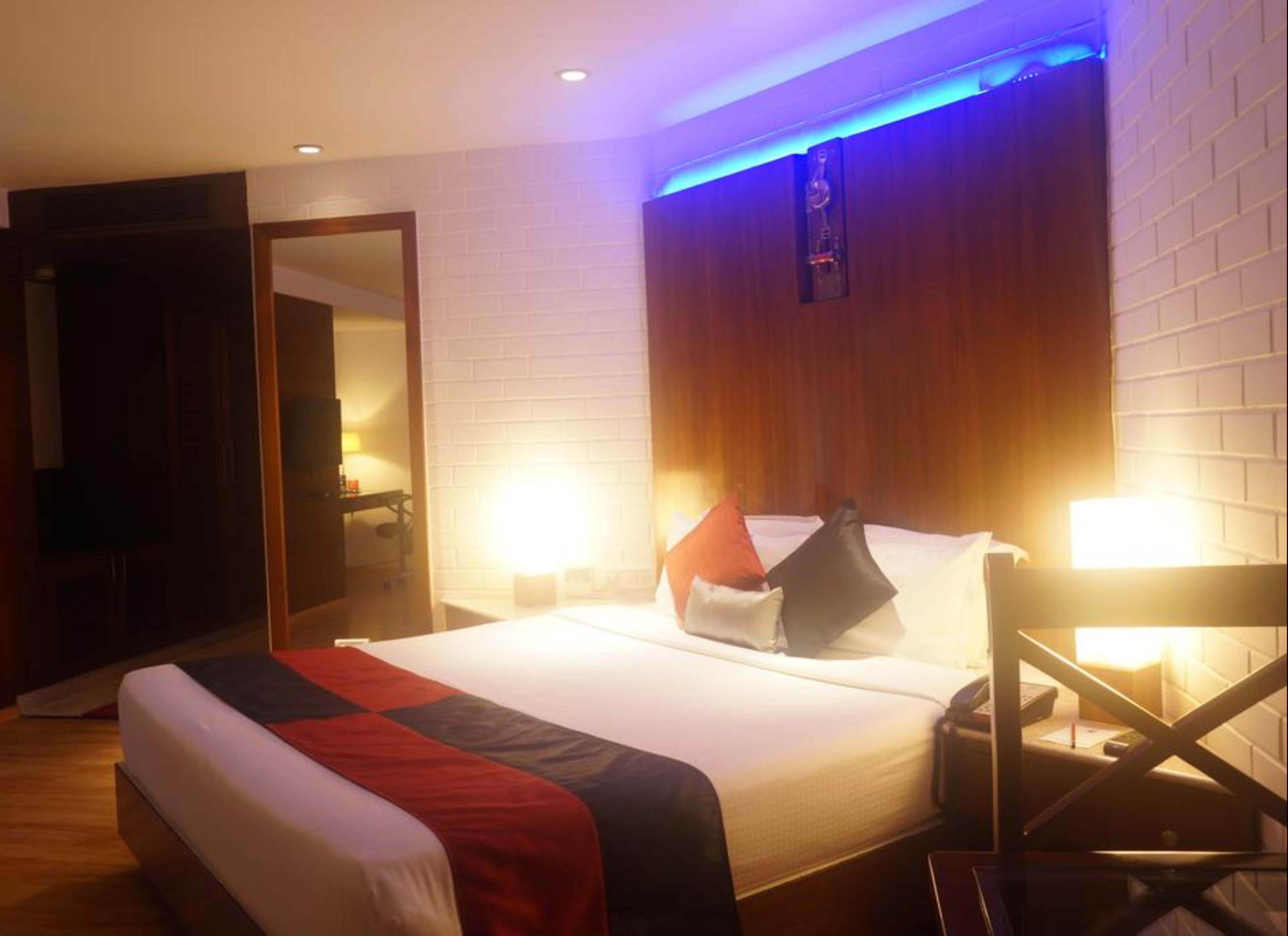 A hotel room with a large bed, a wooden headboard, and a blue accent wall.
