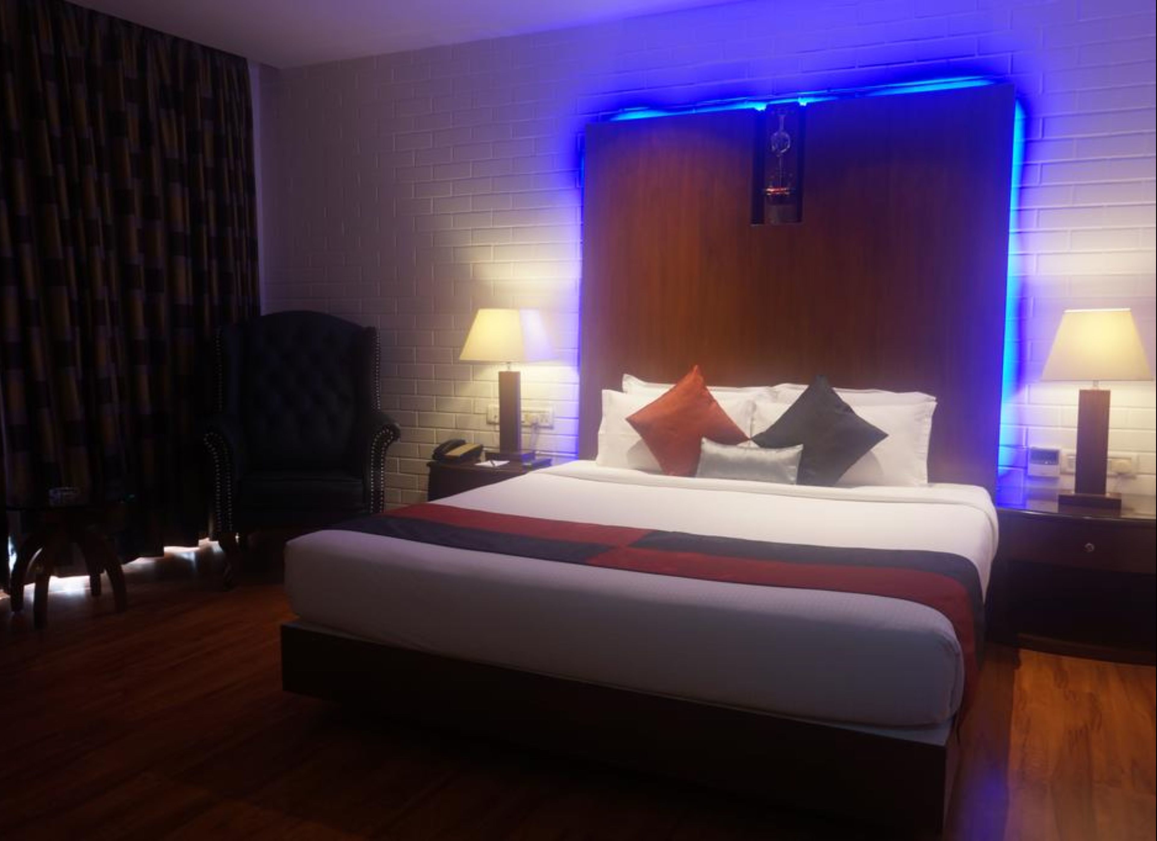 Camera d'albergo con un letto grande, due comodini con lampade, una sedia e un poggiatesta in legno illuminato con luci LED blu.