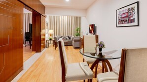A modern hotel room with a wooden floor, a glass dining table, a sofa, and a TV. - SFO Hotel and Suites (Bengaluru)