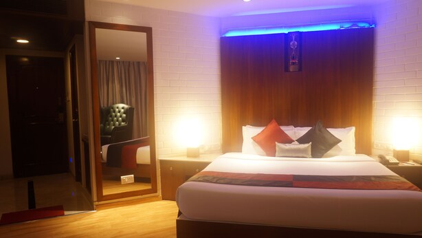 A hotel room with a bed, bedside tables, a mirror, and a wooden headboard. - SFO Hotel and Suites (Bengaluru)