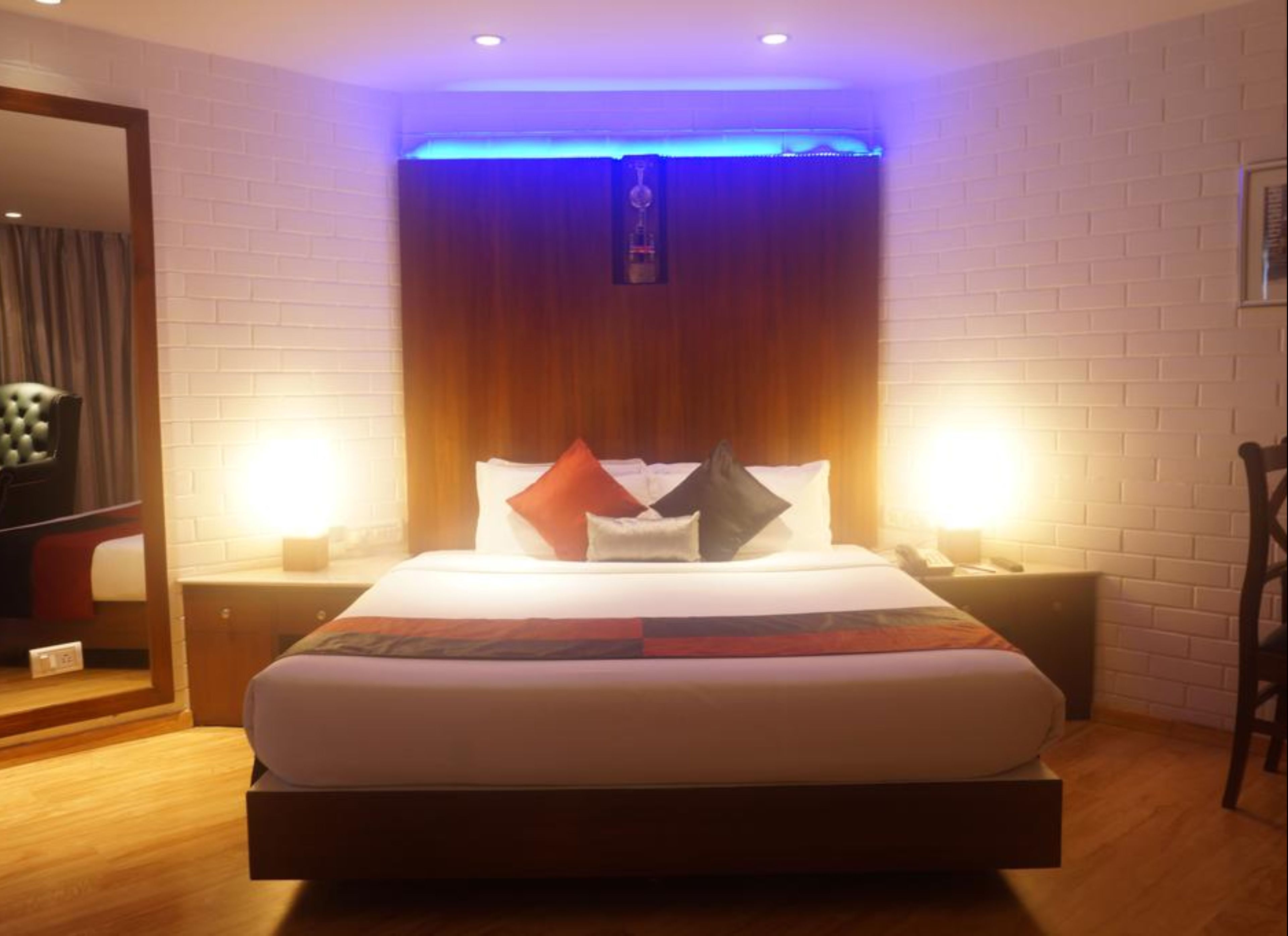 Habitación de hotel con una cama grande, dos mesitas de noche, un cabecero de madera y una lámpara de pared.