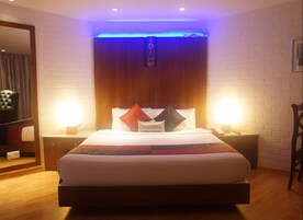 Habitación de hotel con una cama grande, dos mesitas de noche, un cabecero de madera y una lámpara de pared.