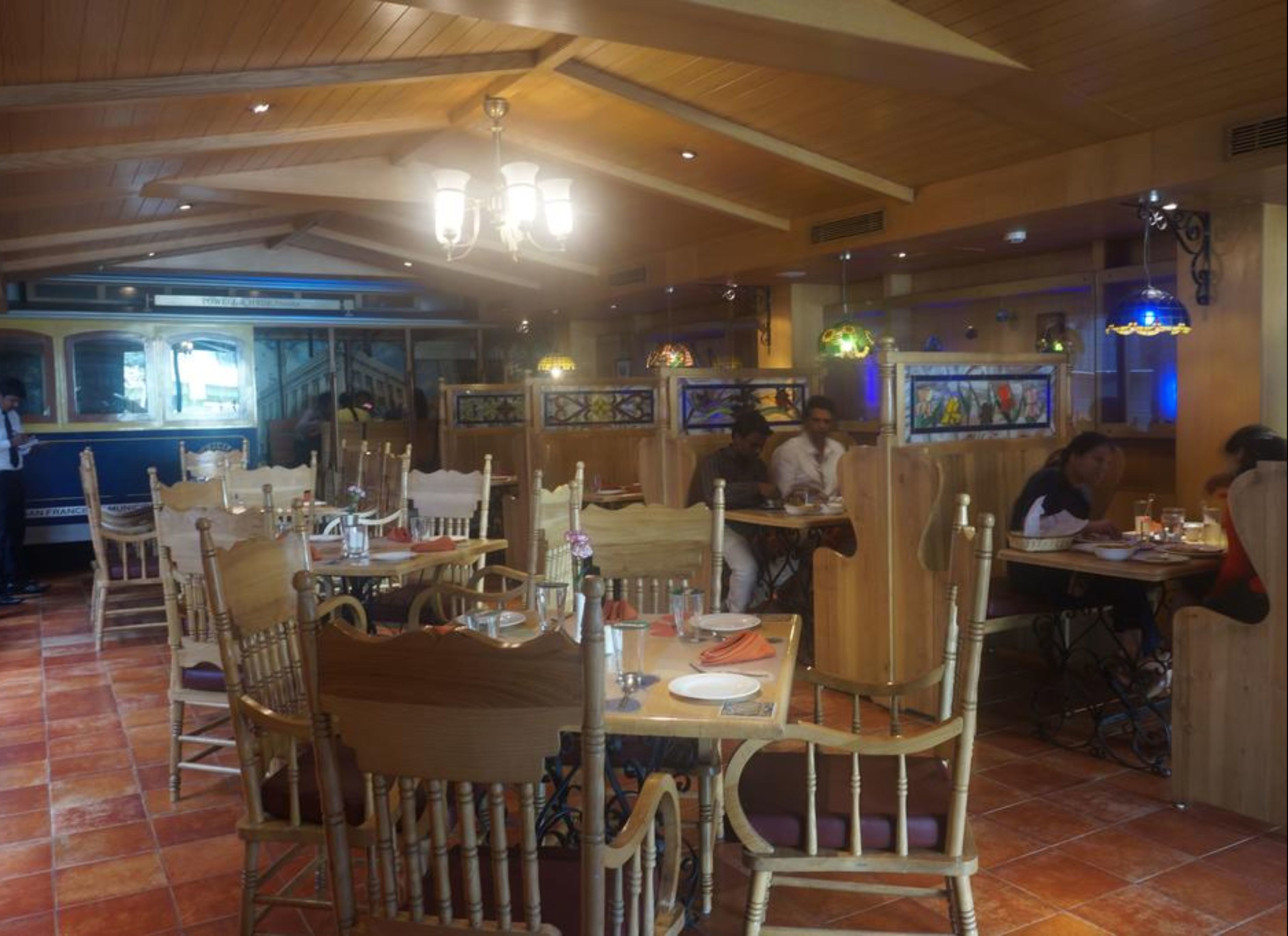 A restaurant with wooden furniture, tiled floors, and a high ceiling with chandeliers.