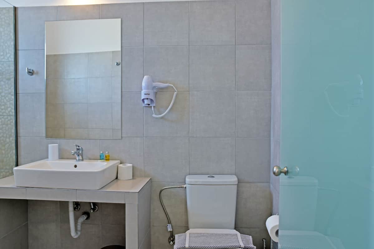 A modern bathroom with a sink, mirror, toilet, and a hairdryer mounted on the wall.