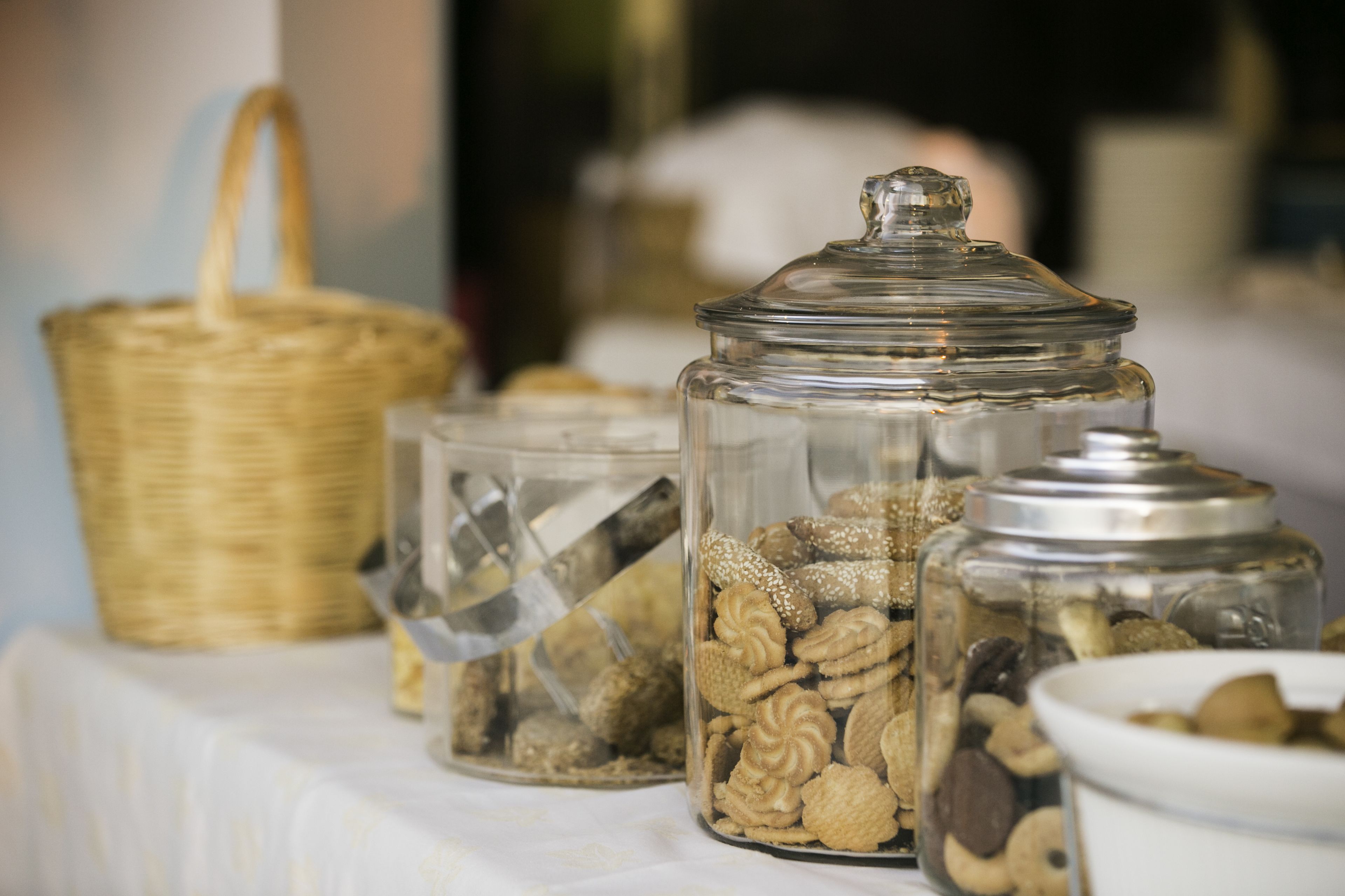 A table with glass jars containing various snacks, a wicker basket, and a white bowl.