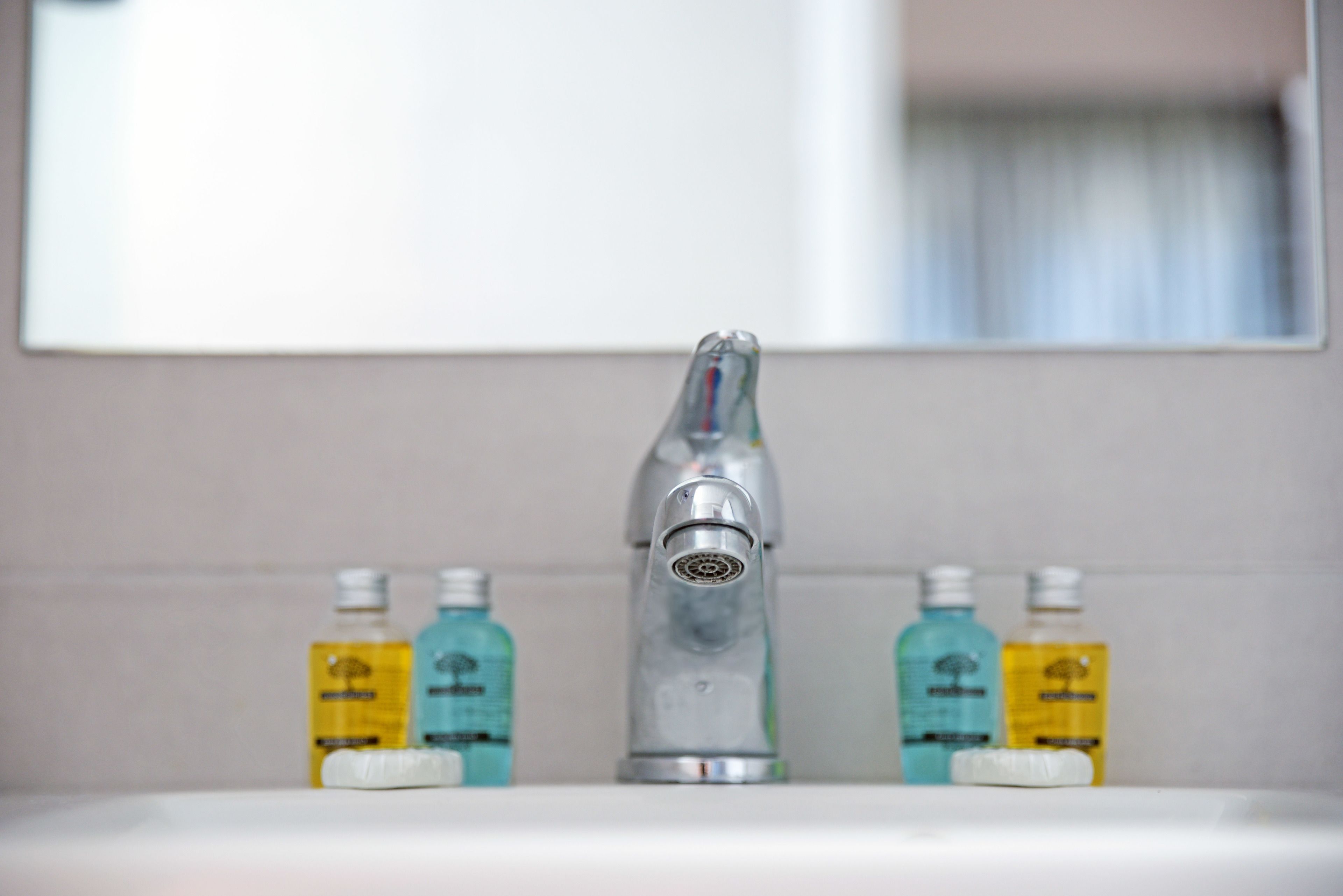A bathroom sink with a modern faucet, two bottles of liquid soap, and a mirror above.