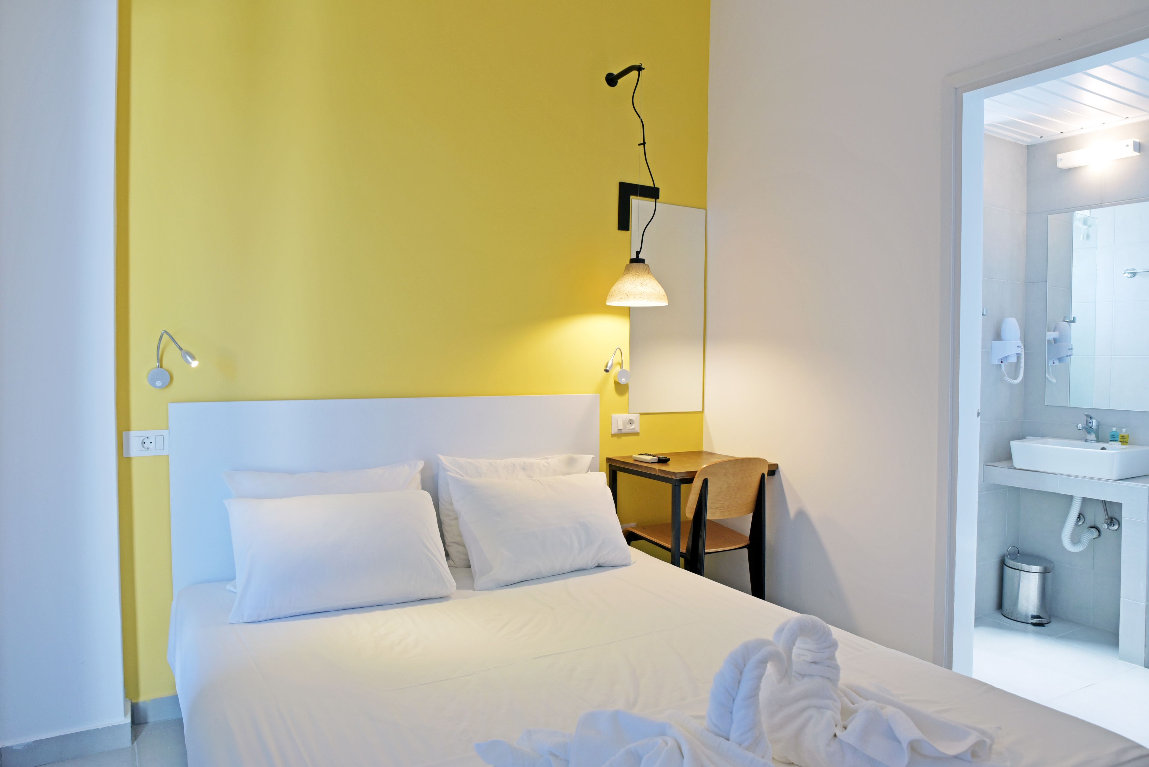 A hotel room with a bed, a desk, a chair, and a bathroom with a sink and mirror.
