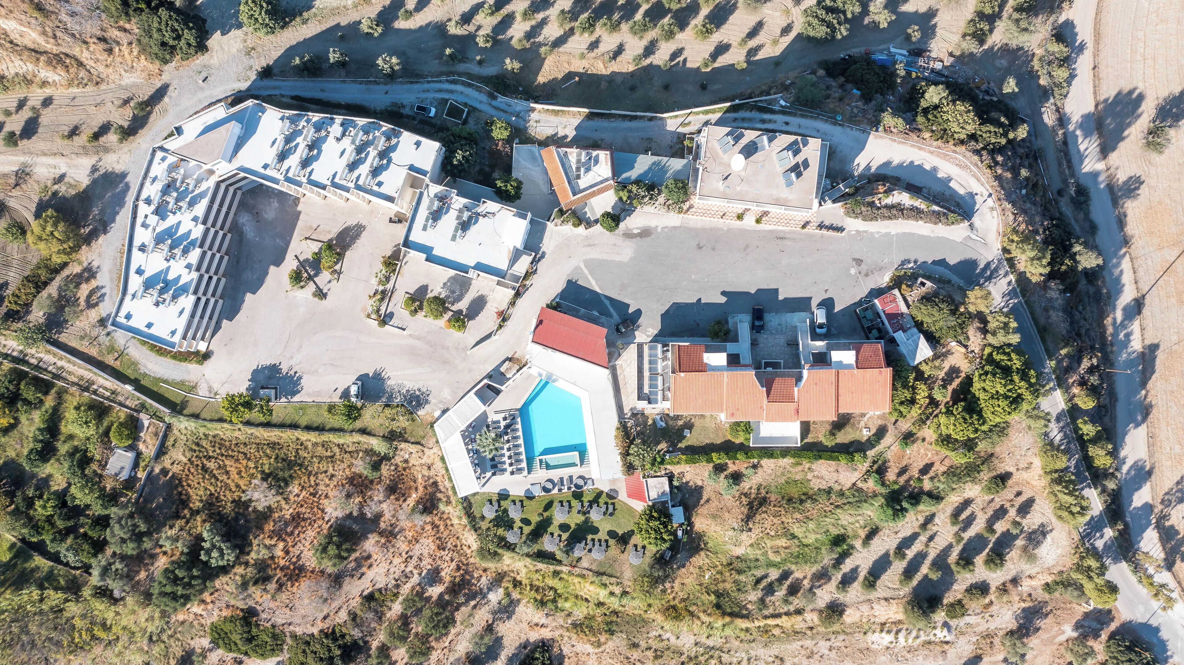 Ett flygbildsbild av ett bostadsområde med flera byggnader, inklusive ett stort hus med ett rött tak, en swimmingpool och flera mindre byggnader.