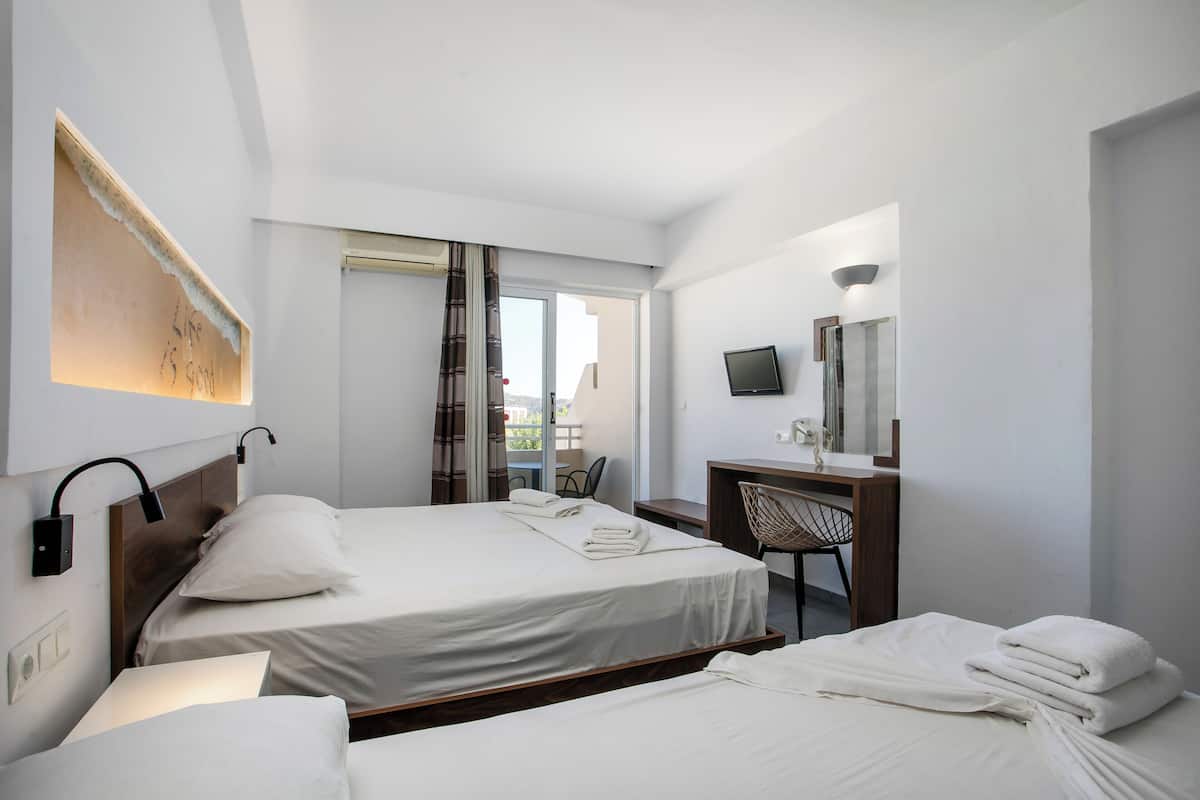 A hotel room with two beds, a desk, a chair, a TV, and a window with curtains.