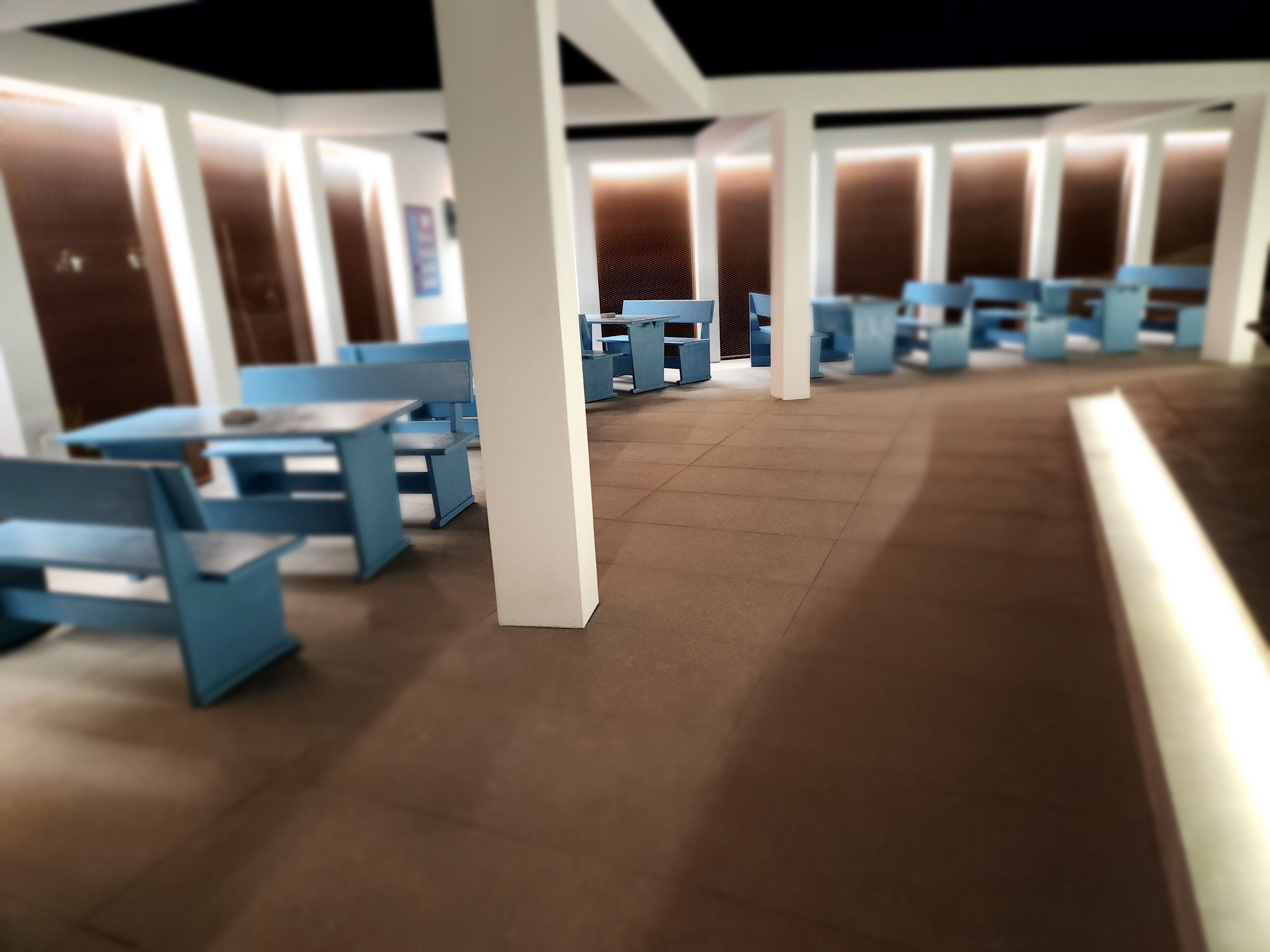 A covered outdoor seating area with blue tables and chairs, a tiled floor, and a series of pillars.