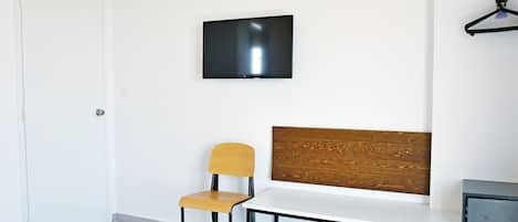 Una habitación moderna con una televisión de pantalla plana montada en la pared, un banco de madera, una mesa blanca y una sola silla.