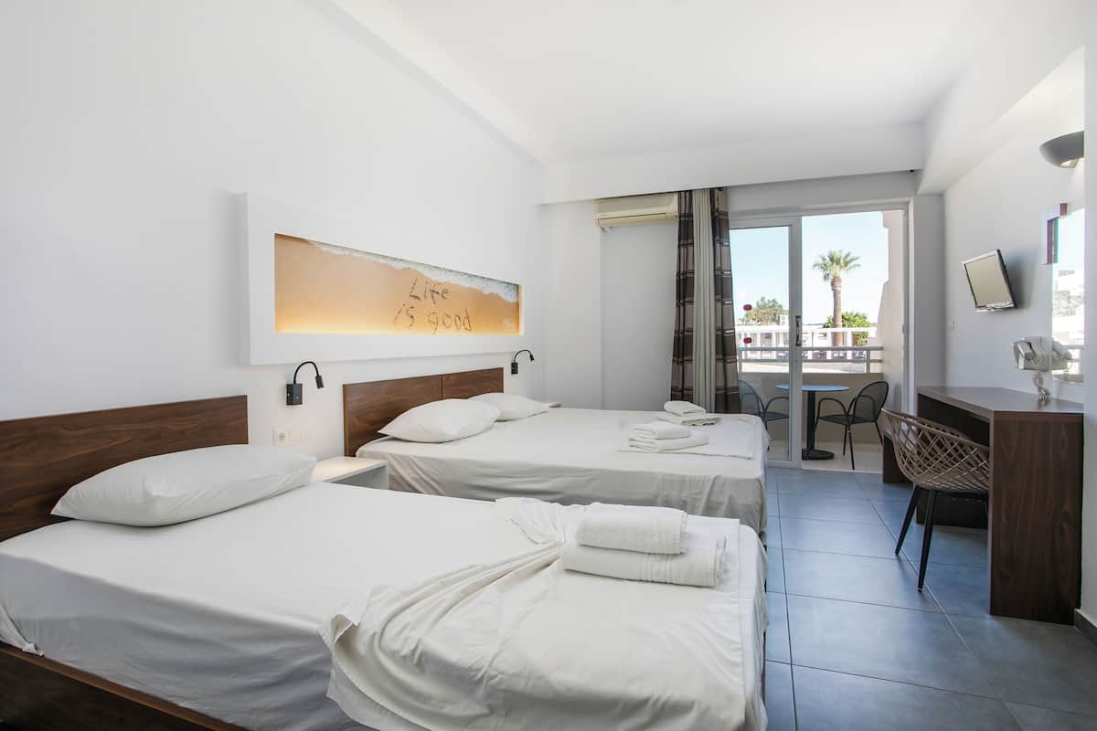 A hotel room with two beds, a desk, and a balcony with a view.