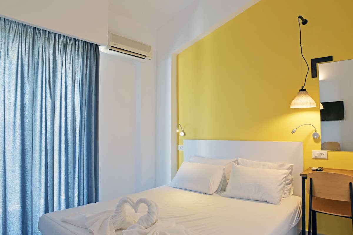 A hotel room with a bed, a headboard, a bedside table, a chair, a lamp, and a curtain.