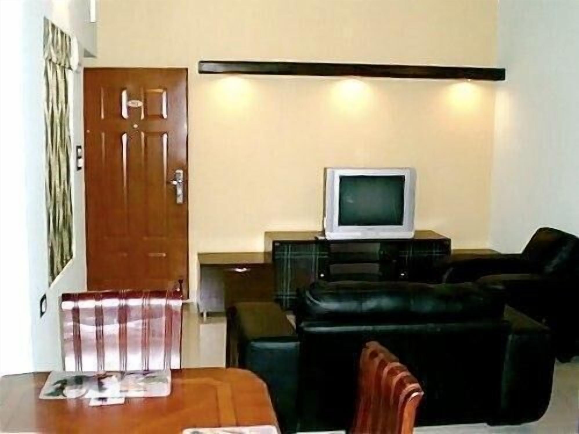 A living room with a television on a stand, a sofa, a table with magazines, and a door.