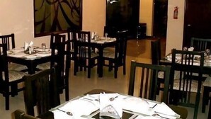 A dining area with tables set for four, chairs, and a large abstract painting on the wall. - Stamford Residency (Bengaluru)