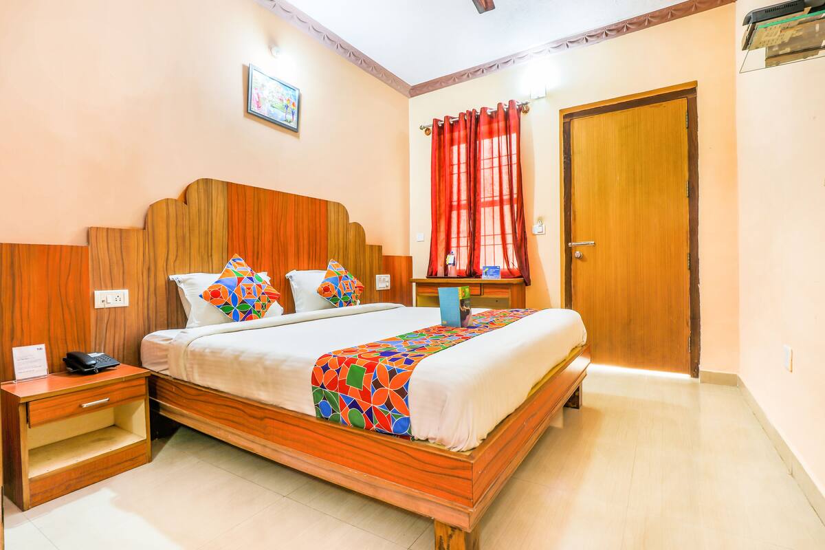 A hotel room with a wooden bed, a nightstand, a desk, a chair, a red curtain, and a door.