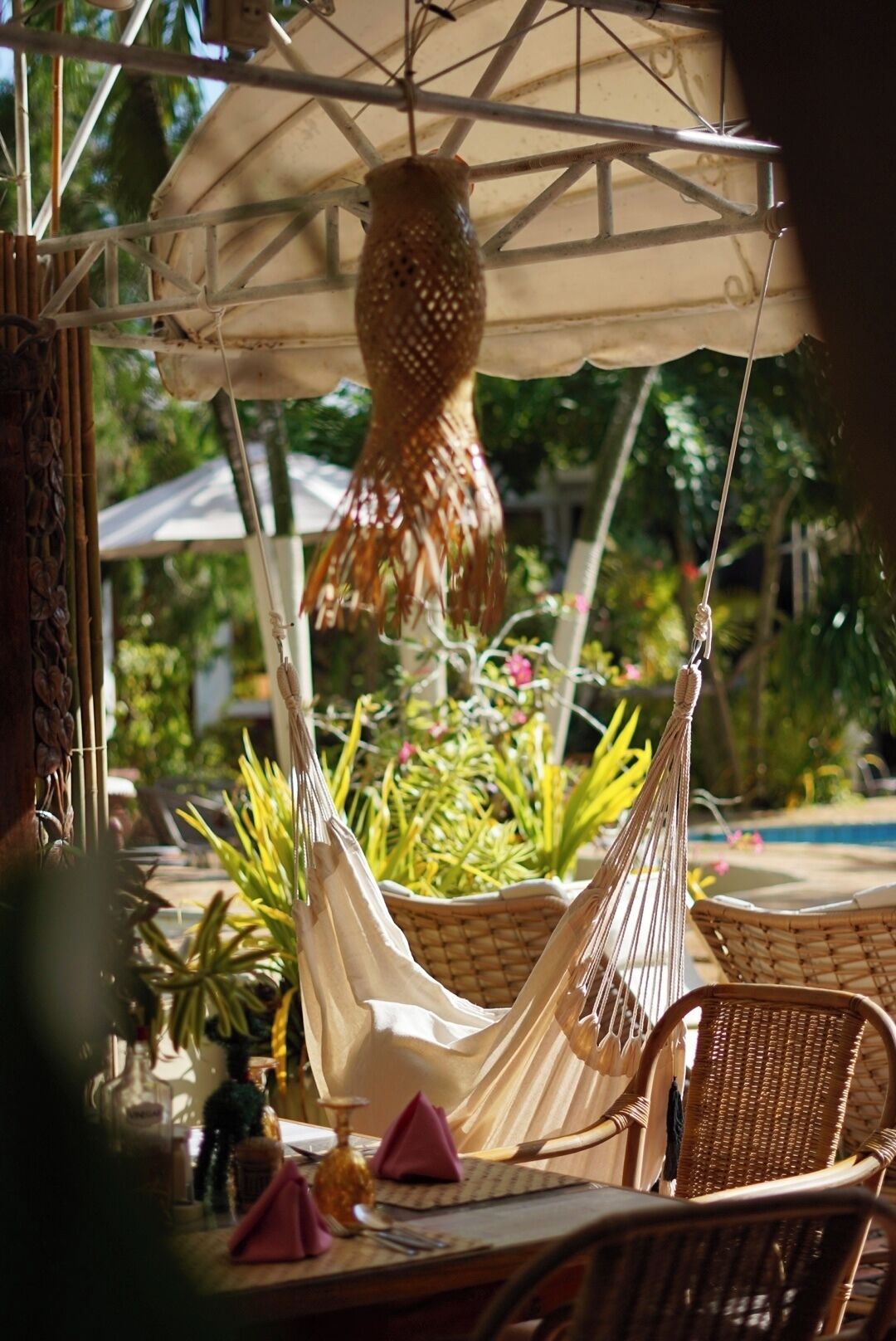 A hammock chair, a table with a placemat, and a hanging decorative item in a garden setting.