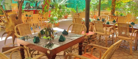 A restaurant with wicker furniture, a glass table, and potted plants.