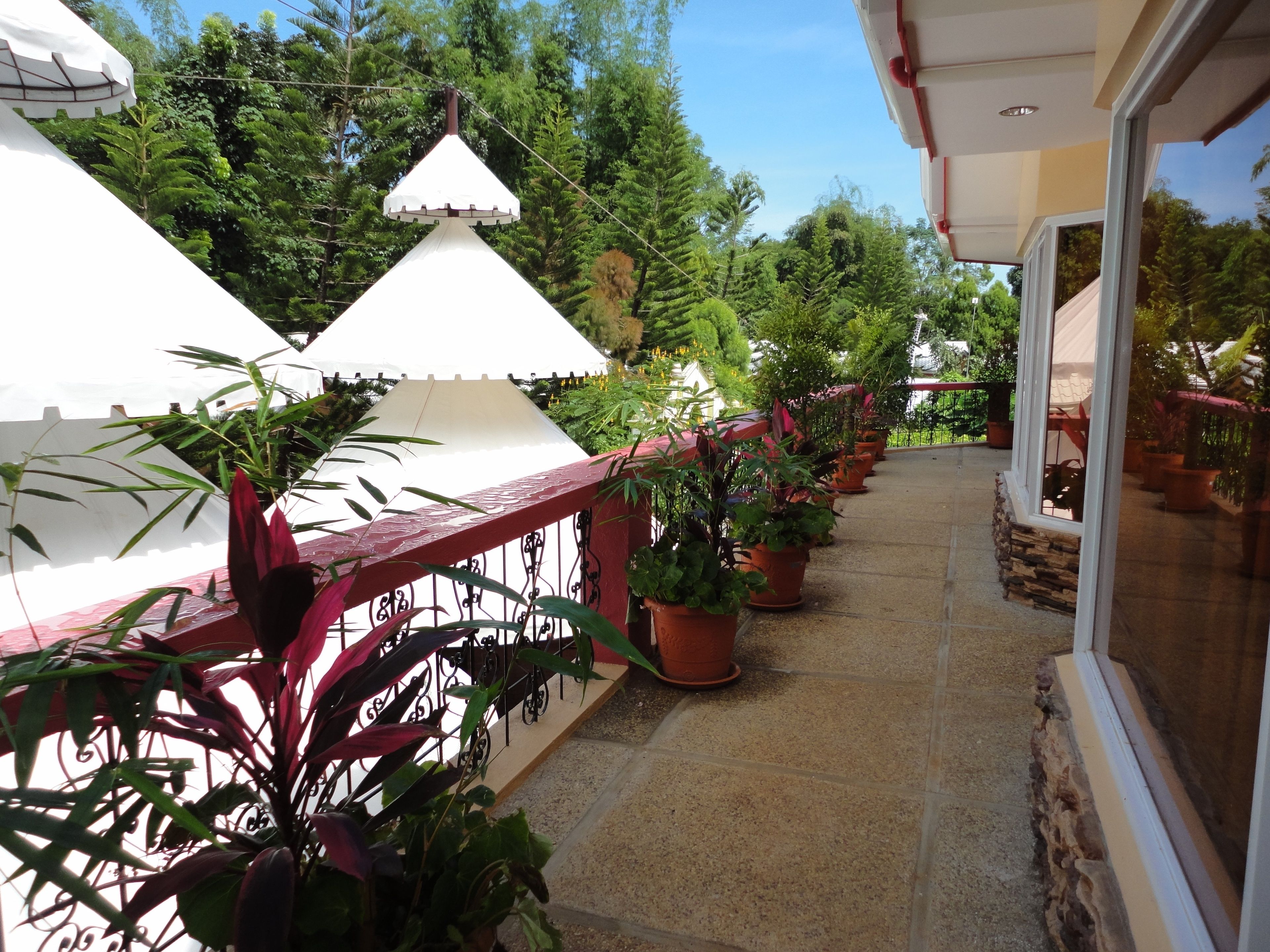 A covered outdoor balcony with potted plants and a red railing.
