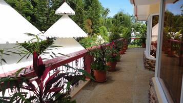 A covered outdoor balcony with potted plants and a red railing.