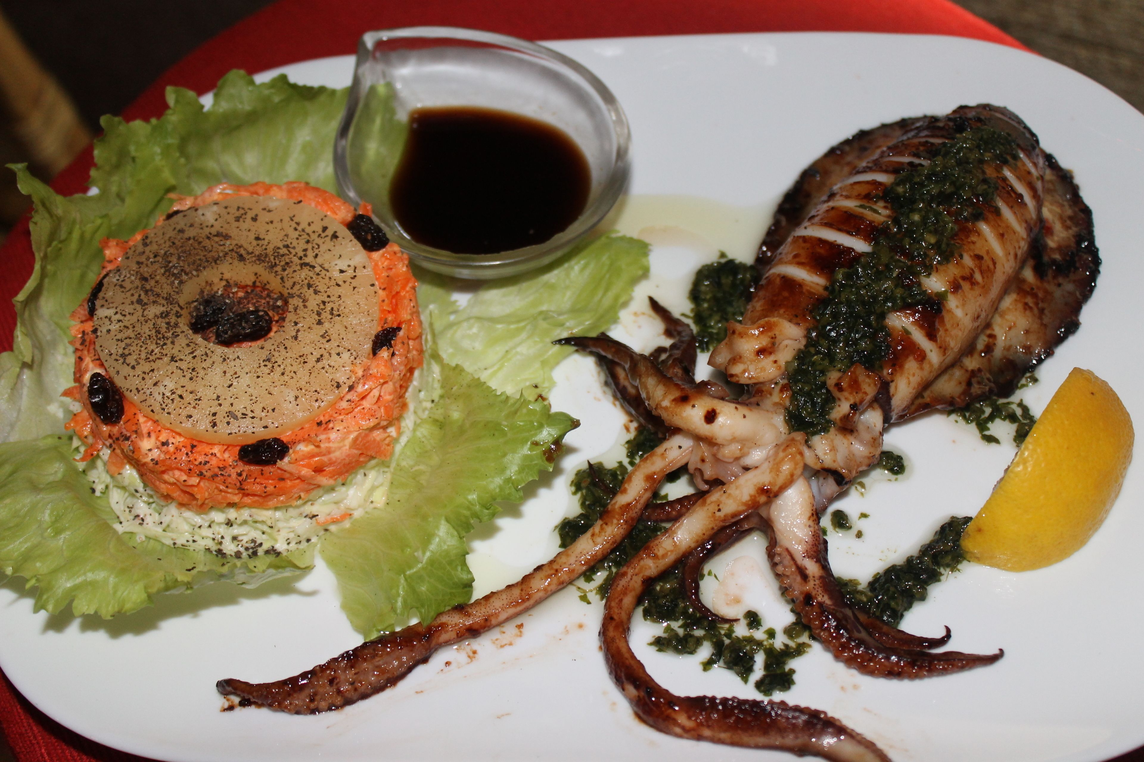 A plate with grilled octopus, a salad, and a lemon wedge.