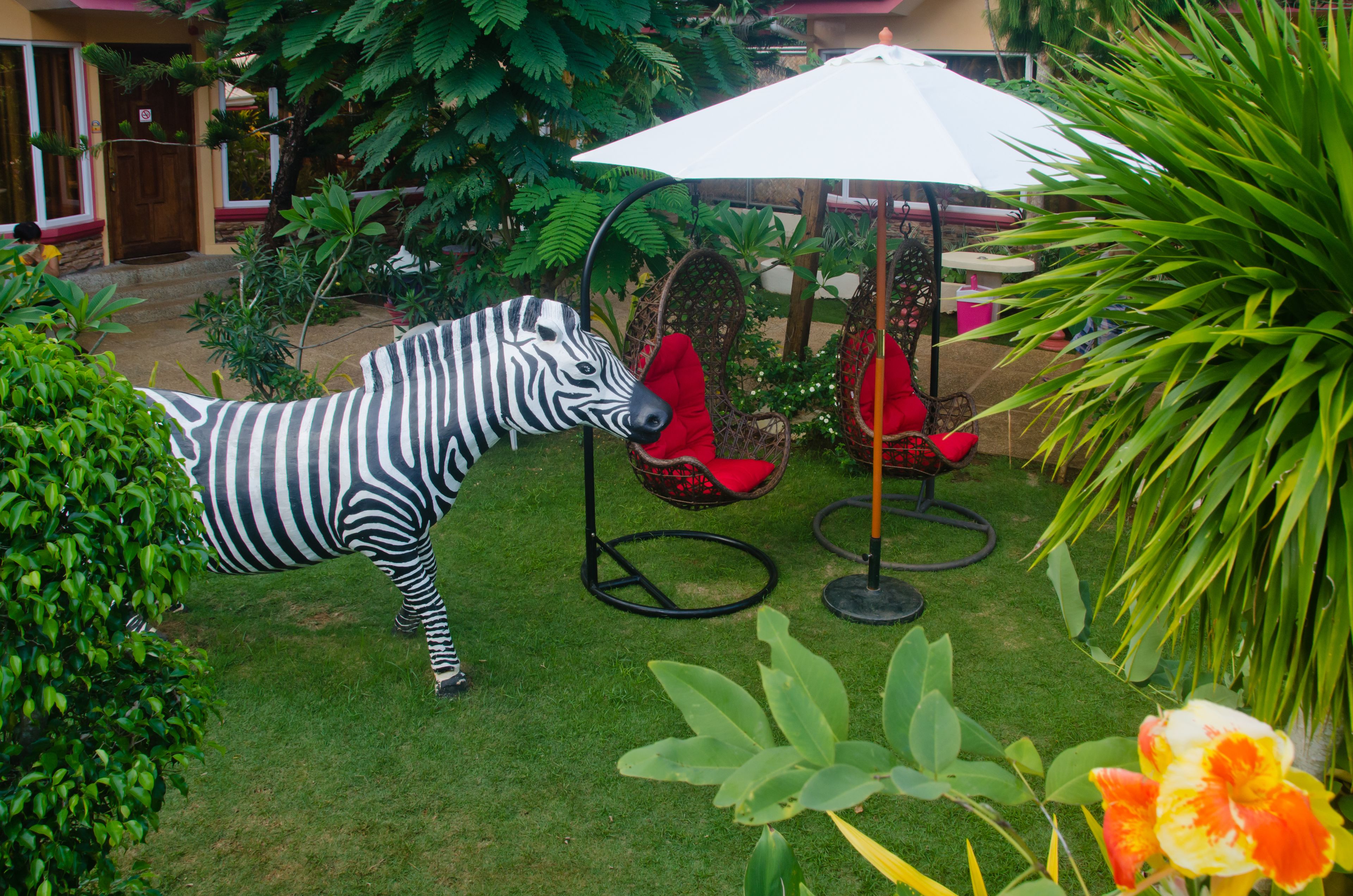 Een zebrapadbeeld in een tuin, met een rode stoel en een witte parasol.