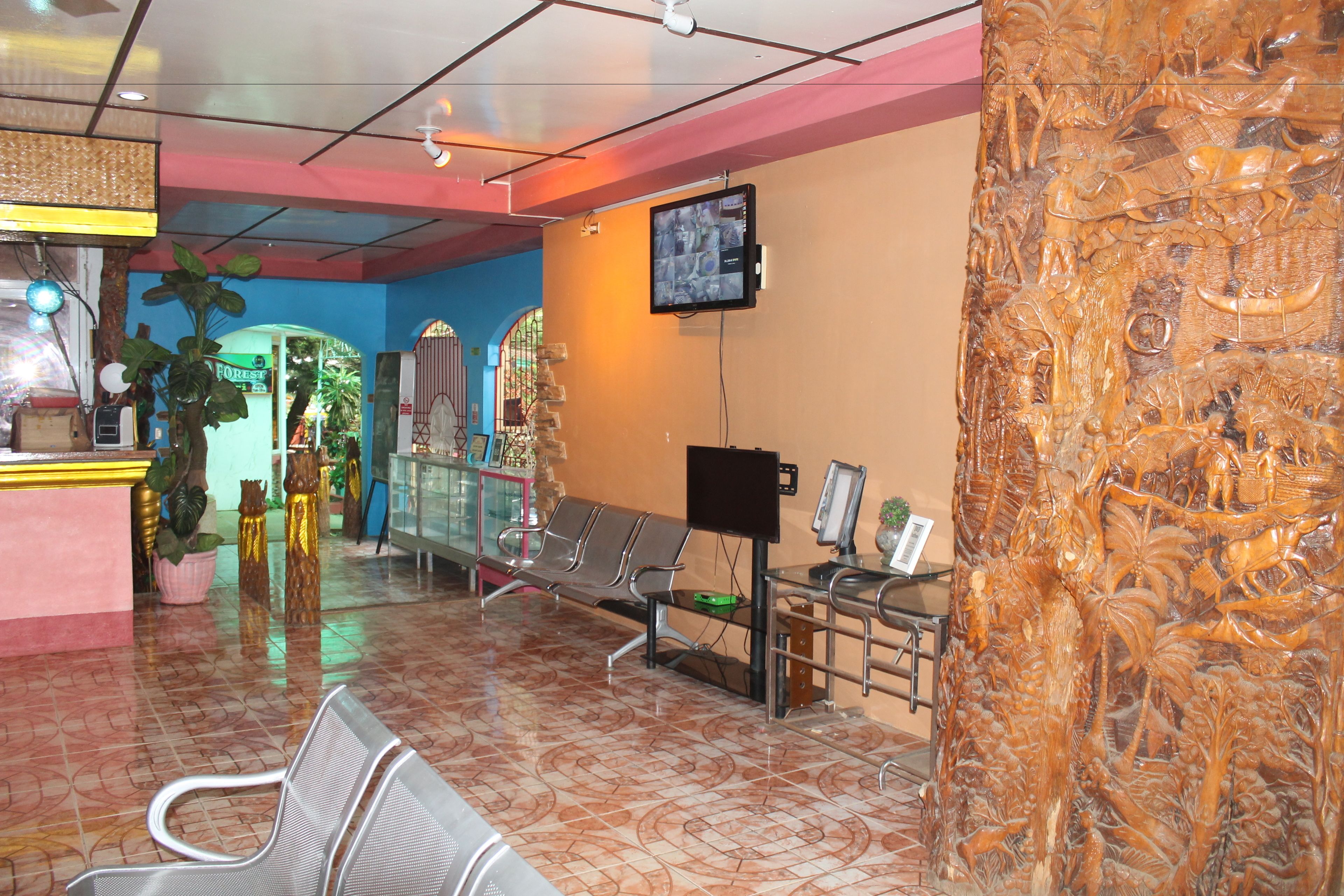Um hall de entrada com balcão de recepção, área de espera com cadeiras, televisão fixada na parede e painel decorativo de madeira.