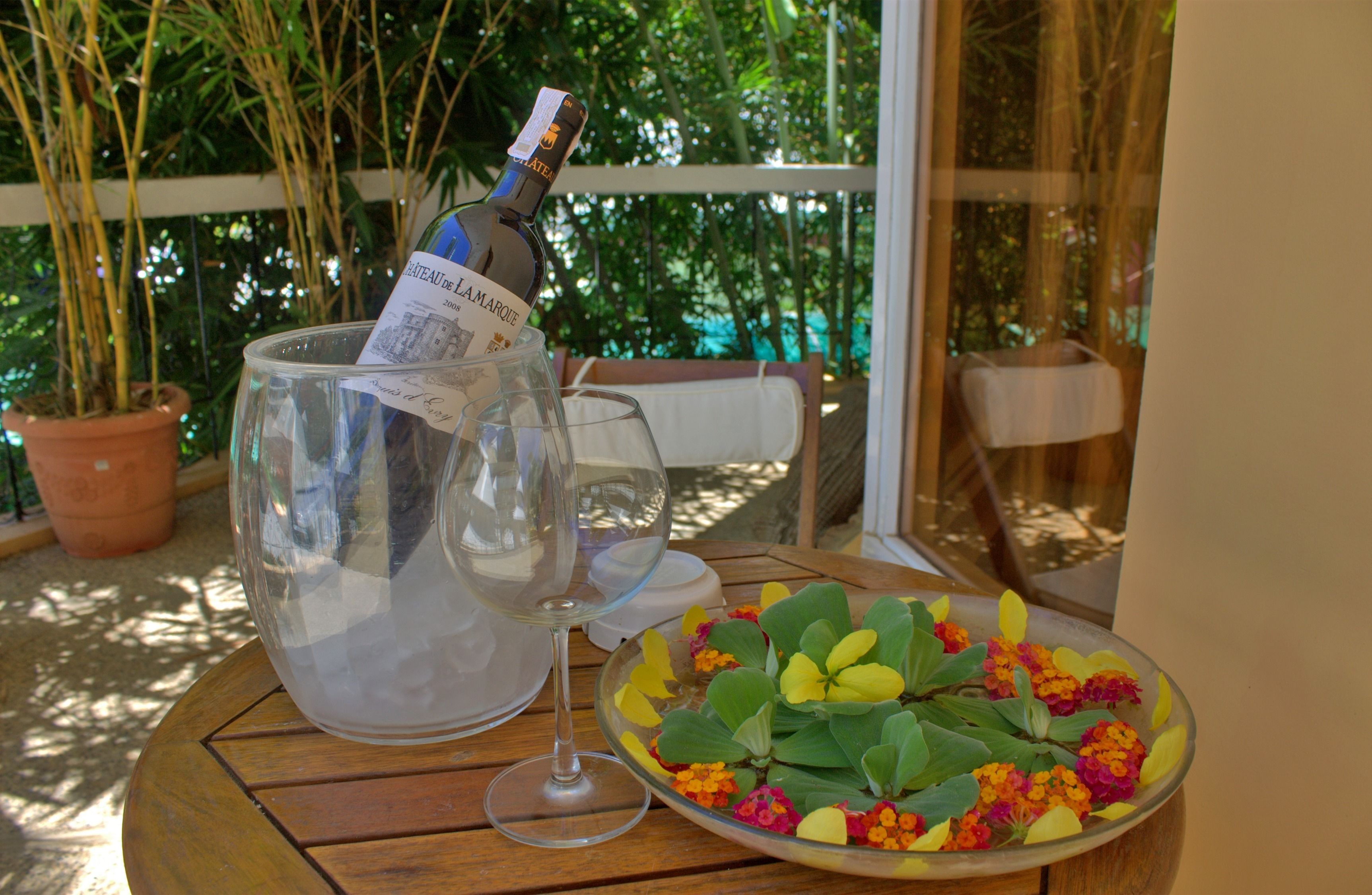 A table with a bottle of champagne, a glass, and a bowl of flowers.