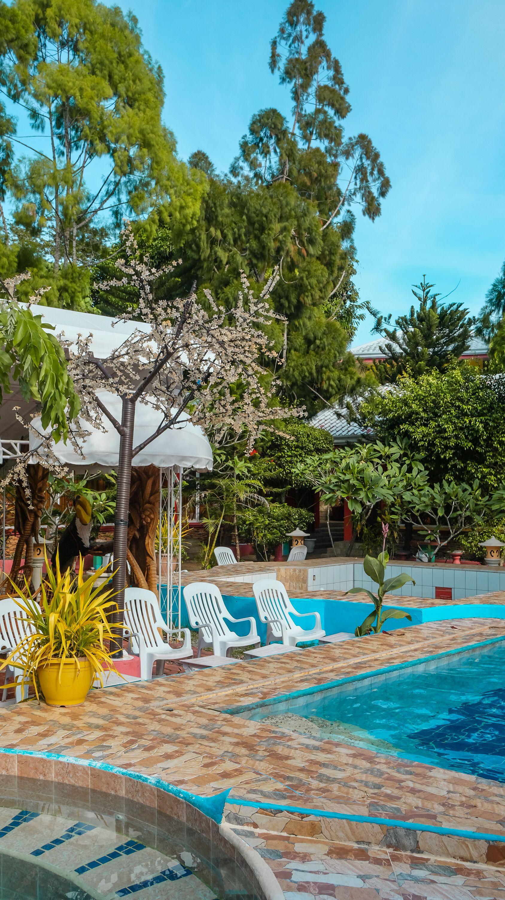 A pool area with white plastic chairs, a tiled deck, and a white umbrella.