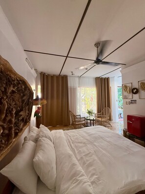 A hotel room with a bed, a ceiling fan, a dining area with chairs, and a red refrigerator. - Deep Forest Garden Hotel (Puerto Princesa)
