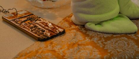 A neatly arranged room with a bed, a plush green towel, a decorative keychain, and a small table with a tissue and an orchid.