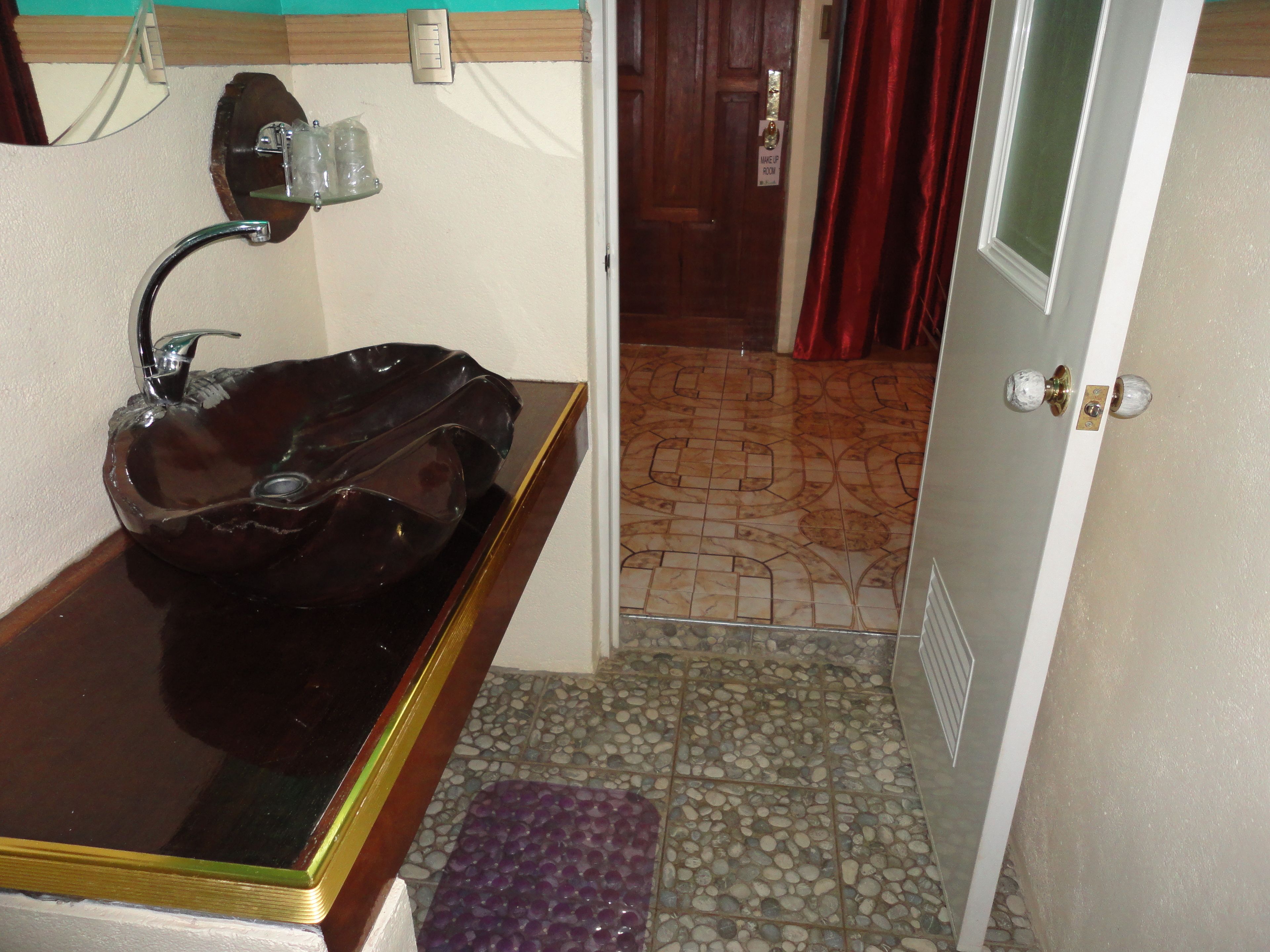 A bathroom with a dark brown sink, a mirror, a towel rack, and a door with a sign reading "MAKE UP ROOM".