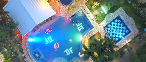 An aerial view of a resort with a large pool, a separate pool area, and a checkered lounge area.