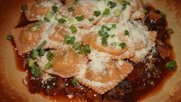 A plate of ravioli with a brown sauce, topped with grated cheese and chopped green onions.