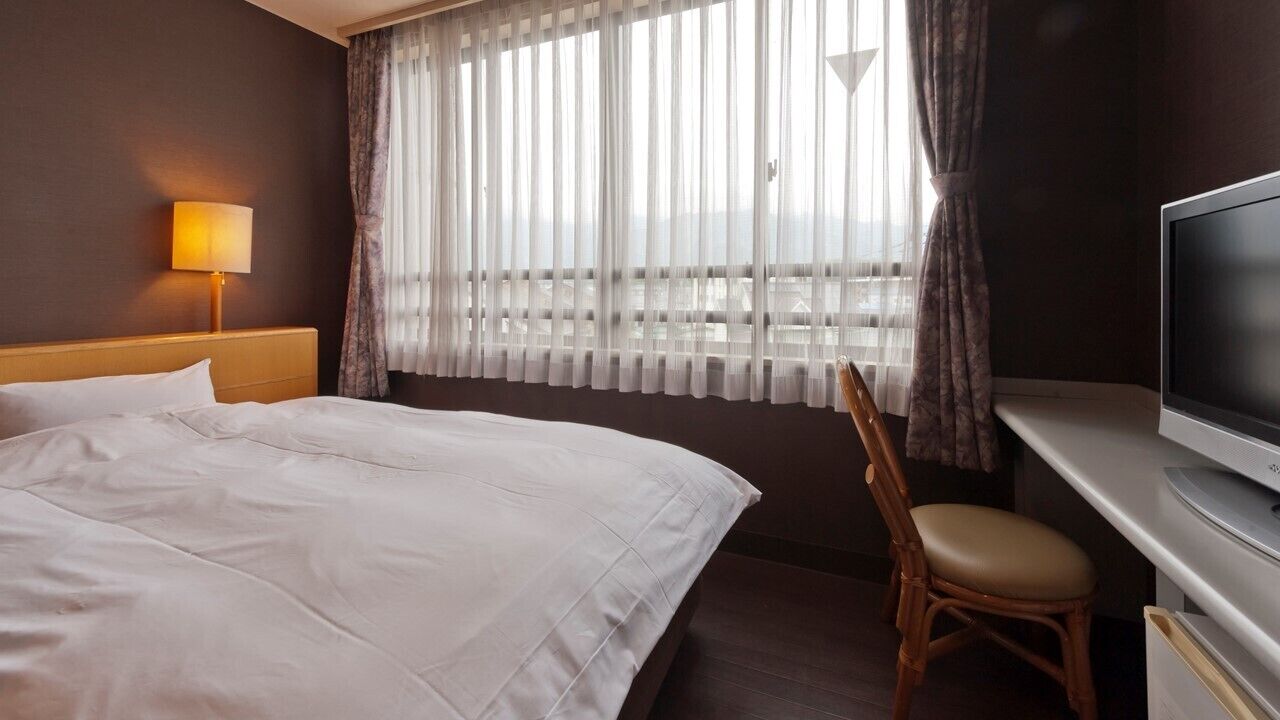 Ett hotellrum med en säng, ett skrivbord med en tv, en stol och ett fönster med gardiner.