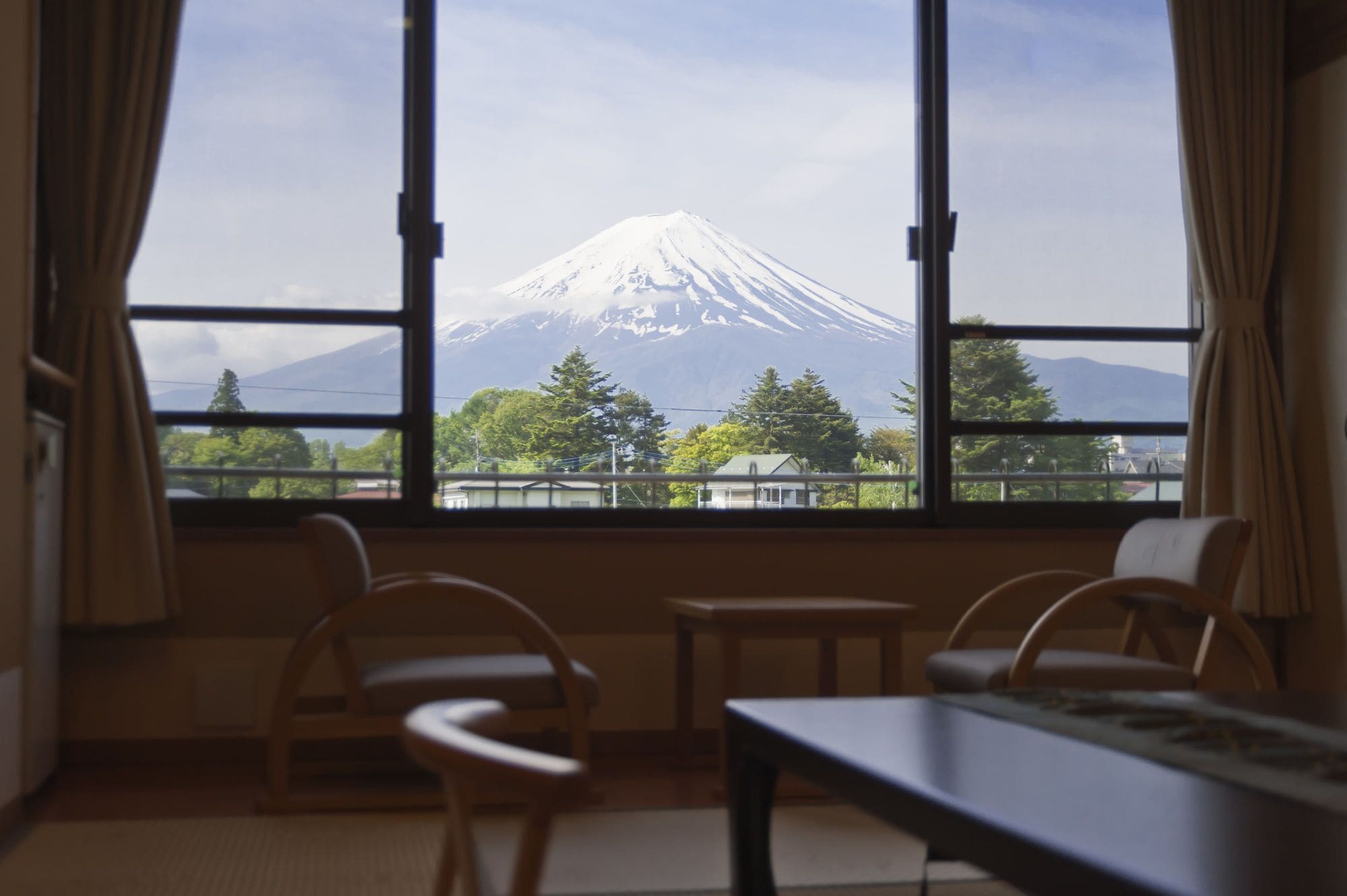 A room with a large window offering a view of Mount Fuji. There are two chairs and a table in the room.