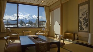 Una habitación japonesa tradicional con suelo de tatami, una mesa baja y sillas. Un ventanal ofrece vistas a una montaña nevada.